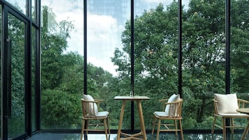 A modern interior with large windows, wooden furniture, and a glass floor reflecting the view of lush greenery outside.