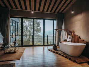 A spacious bathroom with a large bathtub, wooden flooring, and a view of trees through large windows. - Hide and see  (Chongqing)