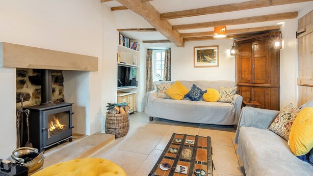A cozy living room with a fireplace, a sofa, a yellow ottoman, and a coffee table with decorative plates.
