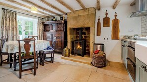 A rustic kitchen with exposed wooden beams, a stone fireplace, and a dining area with a table and chairs.