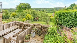 A garden with a stone wall, wooden bench, and potted plants.
