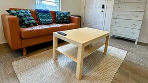 Ein Wohnzimmer mit einem braunen Ledersofa, einem Holztisch und einer weißen Kommode mit Schubladen.
