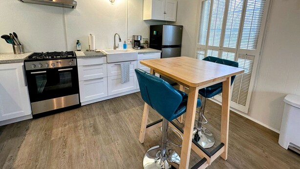 Eine moderne Küche mit Gasherd, Backofen, weißen Schränken, einer Edelstahl-Dunstabzugshaube, einer Kaffeemaschine und einem Kühlschrank.