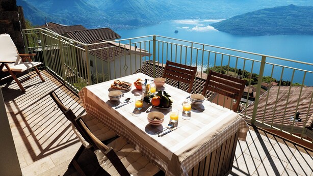 Une terrasse avec une table dressée pour le petit-déjeuner, donnant sur un lac de montagne.