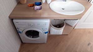 Une petite salle de bain équipée d’un lave-linge, d’un évier et d’un petit espace de rangement.