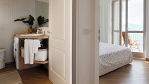 Une chambre à coucher avec un lit, une grande fenêtre donnant sur un beau paysage, une salle de bain avec un lavabo et un miroir, et un plancher en bois.