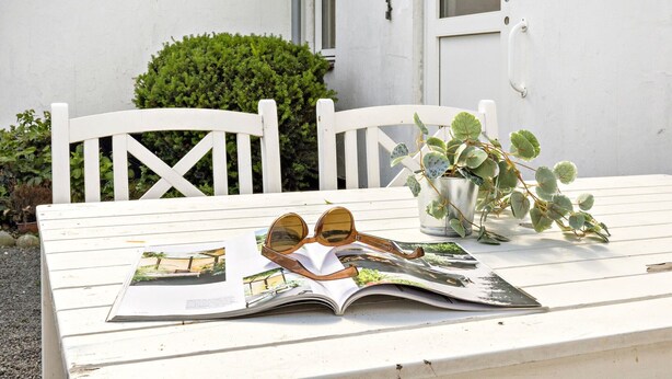 Een witte tafel met een tijdschrift, zonnebril en een bloempot.