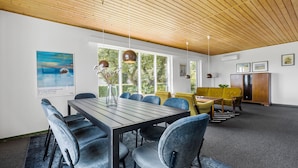 Een moderne eetruimte met een houten plafond, grote ramen en een mix van blauwe en gele stoelen.