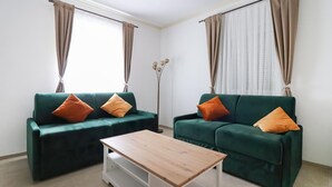 En stue med to grønne sofaer, hver med en orange pude, et træbord og en gulvlampe.