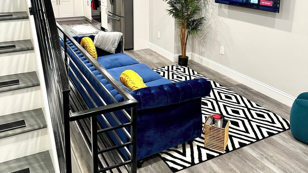 A modern living room with a blue sofa, a TV displaying 'DRAMA', and a staircase leading to a kitchen. - City views roof deck 4B/4B -10 mins to city centre

 (Philadelphia)