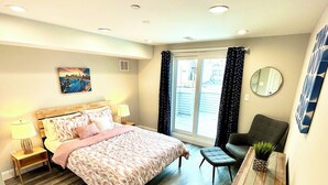 A bedroom with a bed, bedside lamps, a chair, a small table with a plant, a cityscape painting, and a view through the window. - City views roof deck 4B/4B -10 mins to city centre

 (Philadelphia)