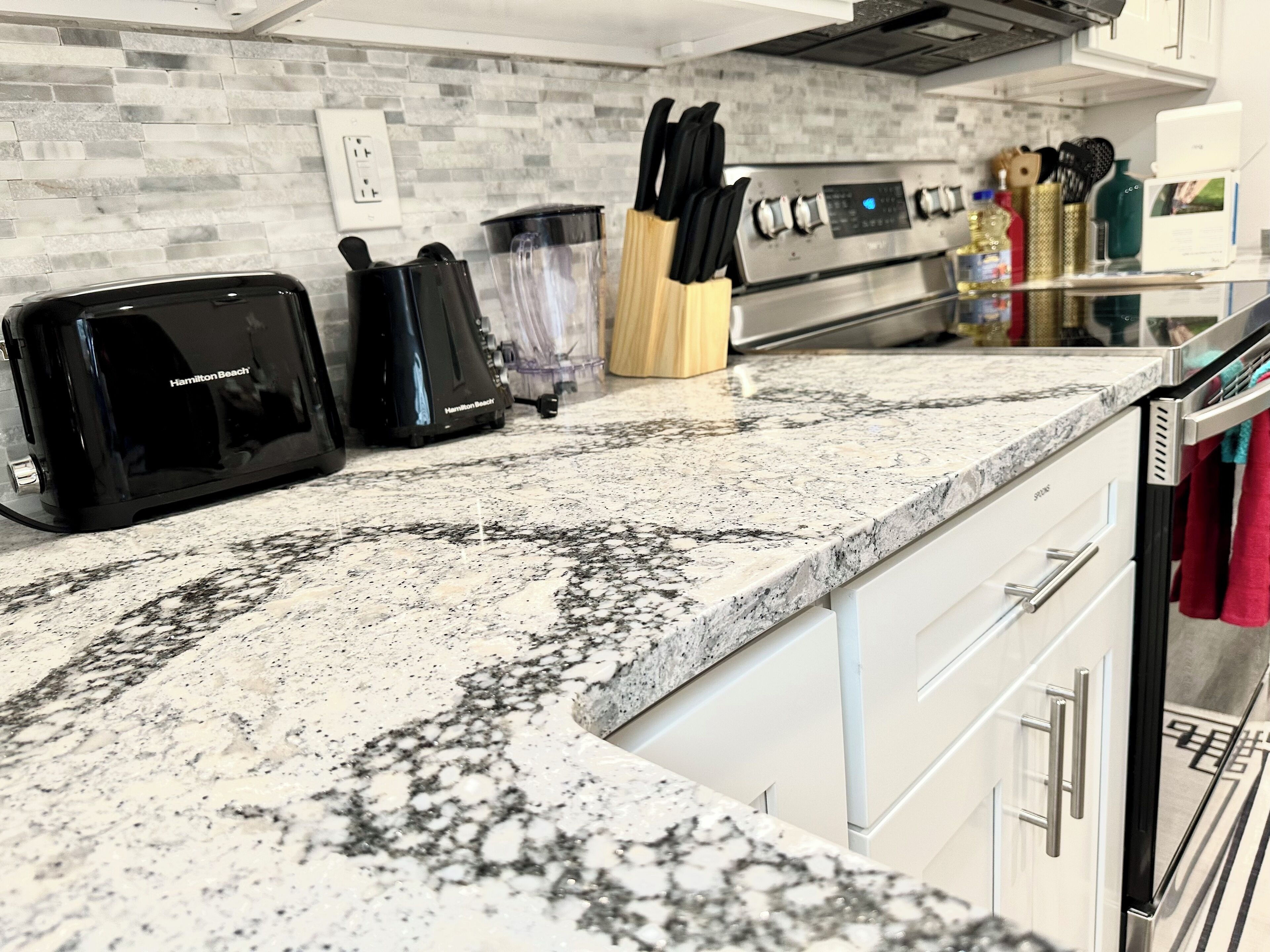 A kitchen with a granite countertop, a Hamilton Beach toaster, a blender, and a knife block.