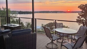 Een balkon met rieten meubels en een tafel, met uitzicht op een wateroppervlak tijdens zonsondergang.