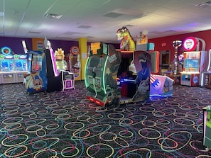 An arcade with various gaming machines, including basketball and racing games, and a dinosaur-themed machine.