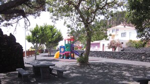 Une aire de jeux avec un toboggan et des structures d’escalade, entourée de tables de pique-nique et d’arbres.