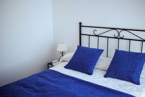 A bed with a white mattress, two blue pillows, a blue blanket, and a black metal headboard. - Rabel House (La Fajana)