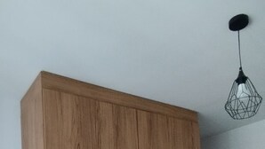 Une chambre avec une armoire en bois, une couvre-lit rouge et un luminaire suspendu.