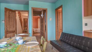 A dining area with a table set for two, a sofa, and a staircase leading to another room.