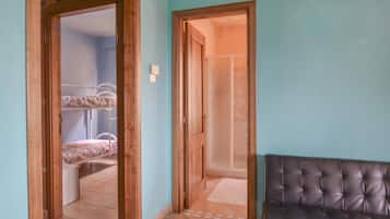 A room with a bunk bed, a wooden door, and a black leather sofa.