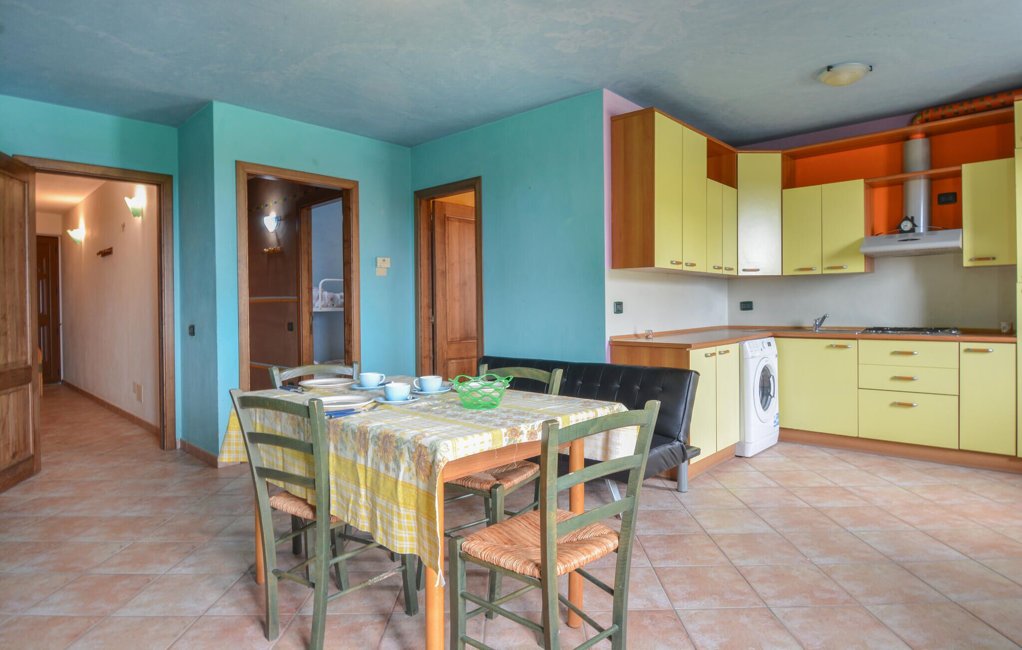 A compact kitchen with a dining area, featuring a table set for four, a washing machine, and yellow cabinets.