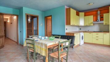 A compact kitchen with a dining area, featuring a table set for four, a washing machine, and yellow cabinets.