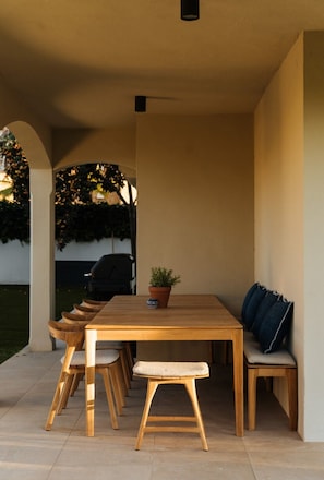 Een terras buiten met een houten tafel en stoelen, een bloempot en een bankje.
