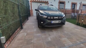 A black SUV parked in a gated driveway with a tiled floor, a metal fence, and a building with a white facade and windows in the background.