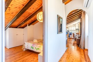 Un dormitorio con techo de madera, una cama con colcha estampada y un pasillo que conduce a una cocina.