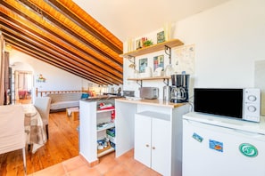 Una cocina compacta con vigas de madera, microondas, cafetera y un refrigerador pequeño.