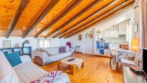 Ett mysigt rum i loftstil med ett träpanelat tak, en soffa, ett litet bord och ett köksområde som syns genom en öppen dörr.