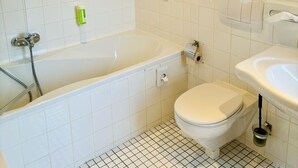 A bathroom with a bathtub, toilet, and sink. There are two potted plants on the wall. - Themenhotel Rehlein (Thale)