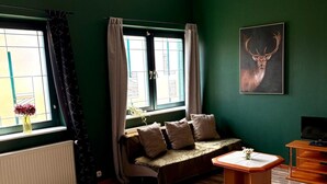 A cozy room with a green wall, a sofa, a small table, and a painting of a deer. - Themenhotel Rehlein (Thale)