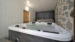 Een bubbelbad in een ruimte met witte panelen, een stenen muur en een houten plank.