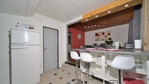 Een compacte keuken met een koelkast, een eethoek met barstoelen en een rode accentmuur.