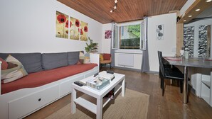 Een woonkamer met een bank, een salontafel met gezelschapsspellen, een eethoek met tafel en stoelen, en kunstwerken aan de muur.