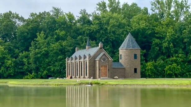 A stone building with a clock tower and a door, surrounded by a pond and trees. -  Hogwarts Themed Castle!  10 Acres - An Amazing Experience! (Westfield)