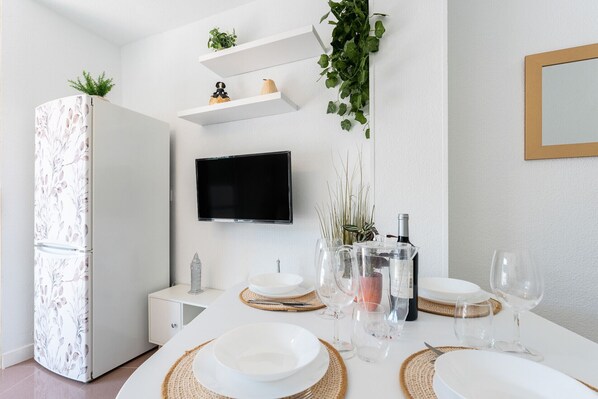 A modern kitchen with white cabinetry, a built-in TV, and a dining area set with white plates and wine glasses.