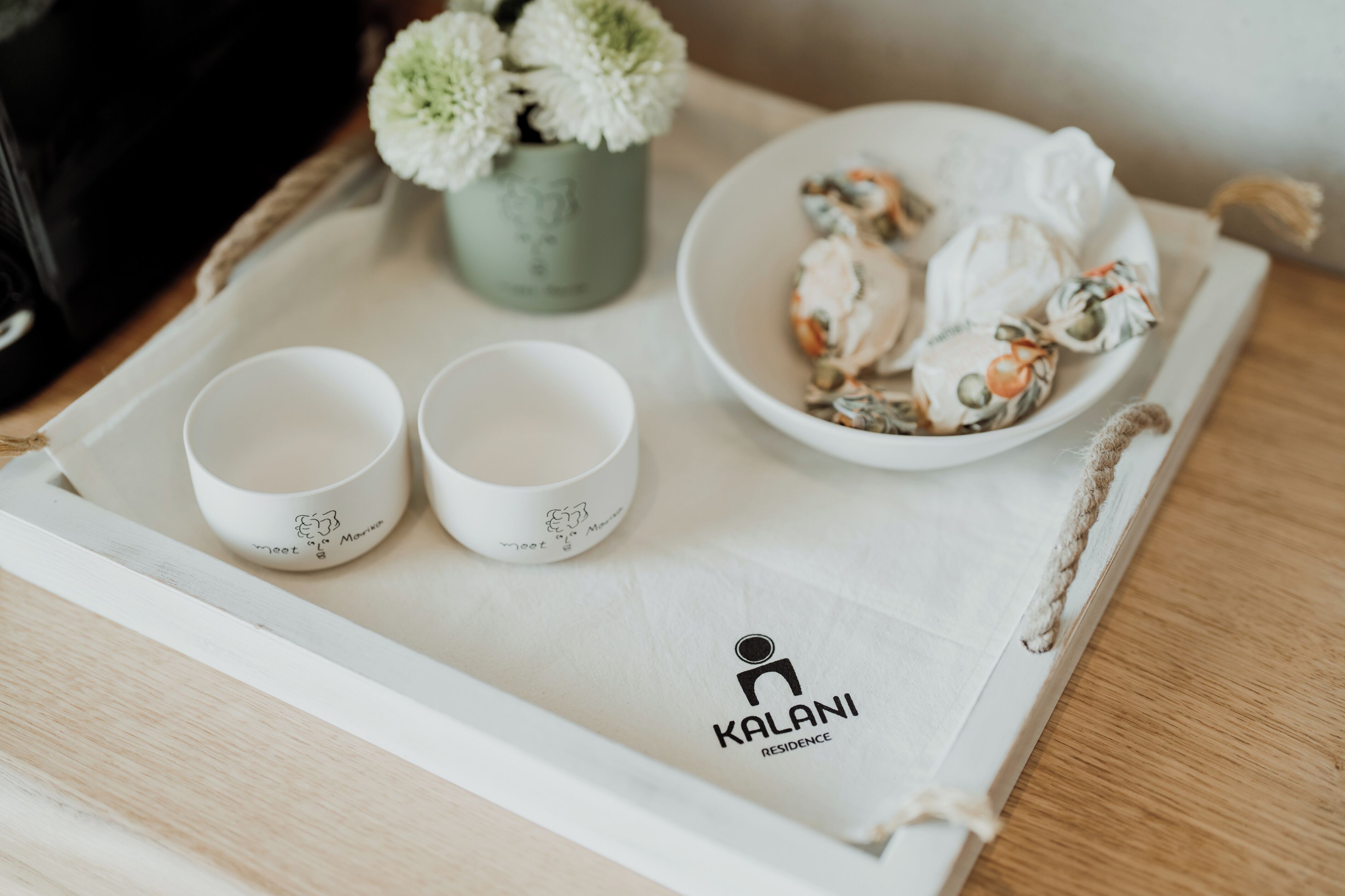 A tray with two white cups, a bowl of pastries, and a small potted plant on a wooden table.