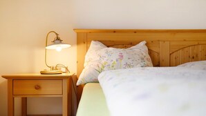 Ein Nachttisch aus Holz mit Lampe, ein Bett mit floralem Bettbezug und ein Holz-Kopfteil.