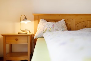 Une table de chevet en bois avec une lampe, un lit avec une literie à motifs floraux et une tête de lit en bois.