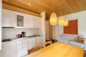 Une cuisine moderne avec des meubles blancs, une machine à café et un coin repas comprenant une table et des chaises en bois.