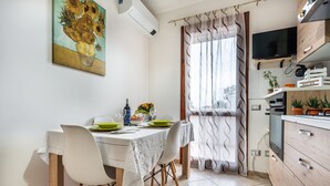 Un coin repas avec une table dressée pour quatre personnes, un tableau accroché au mur et un téléviseur dans la pièce adjacente.