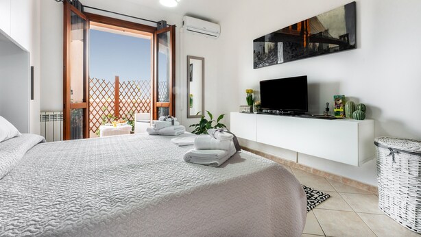 Une chambre avec un lit, une télévision, une console blanche, un panier en osier et une vue sur l’extérieur, visible à travers une porte.