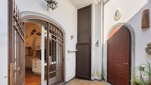 En smal indgang med en lukket brun dør, en tremmeport og en hvid mur med et våbenskjold.