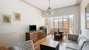 Una sala de estar con un sofá, una mesa de centro, un televisor y un comedor con sillas.