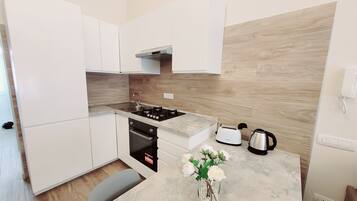 A modern kitchen with white cabinets, a gas stove, a toaster, and a kettle.