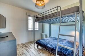 A bunk bed with a ladder, a desk with a remote control, a radiator, and a window with bars.