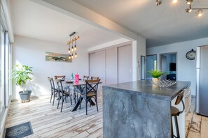 A modern kitchen with a marble island, wooden chairs, a dining table, and a potted plant.