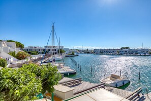 A marina with boats docked, a wooden pier, and buildings in the background.