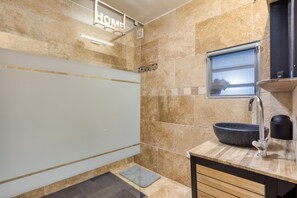A bathroom with a stone wall, a sink with a bowl, a shower, and a 'HOME' sign.
